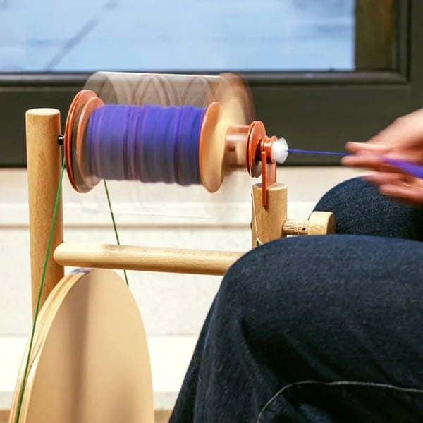 Nahaufnahme des Lojan Buddy Doppeltritt Spinnrads beim Spinnen von lila Garn, laufende Spule mit ruhigem Einzug und ergonomischer Handführung