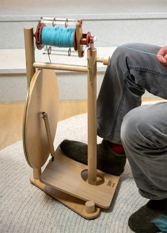 Lojan Buddy Spinnrad in Anwendung, Person spinnt mit breitem Einfachtrittbrett, naturbelassenes Holzrad mit laufender Spule in Handarbeit